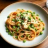 A bowl of Pasta with Peas, garnished with grated Parmesan cheese, presented on a rustic wooden table.