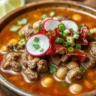 A bowl of Carne en su Jugo, garnished with cilantro, radishes, and green onions, served in a rustic bowl with tortillas on the side.