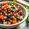 Dense Bean Salad Recipe in a rustic white ceramic bowl with kidney beans, black beans, chickpeas, and fresh vegetables, presented on a wooden table.