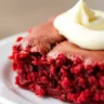 A red velvet brownie with cream cheese frosting on a white plate.