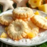 Featured image of Hawaiian Shortbread Cookies on a plate with coconut flakes and pineapple pieces, set against a tropical background.