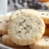 Plate of freshly baked lavender shortbread cookies with lavender buds on top and a cup of tea in the background.