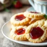 Plate of shortbread cookies with jam, garnished with fresh berries and accompanied by a cup of tea.