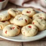 A plate of freshly baked strawberry shortbread cookies with bits of strawberry and light frosting on a rustic wooden table.