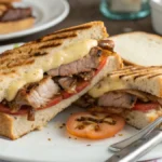 Primer plano de un sándwich de carne con queso casero, con queso derretido y pan dorado, servido sobre una mesa rústica.