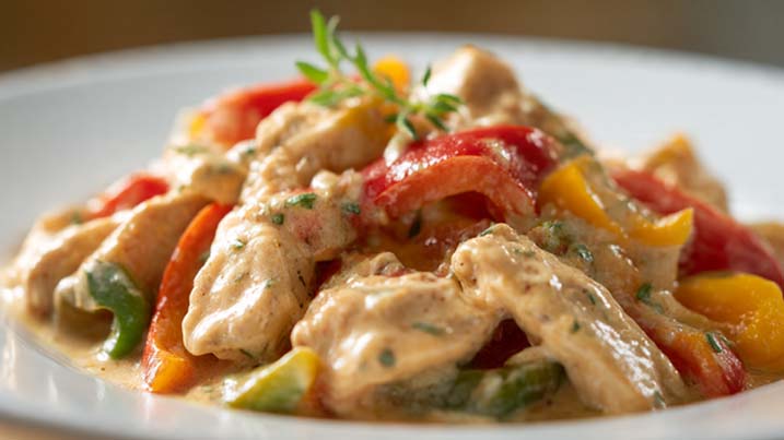 Zartes Hähnchen Geschnetzeltes mit Paprika Sahne Sauce in cremiger Sauce mit frischer Paprika, serviert mit Reis auf einem weißen Teller.