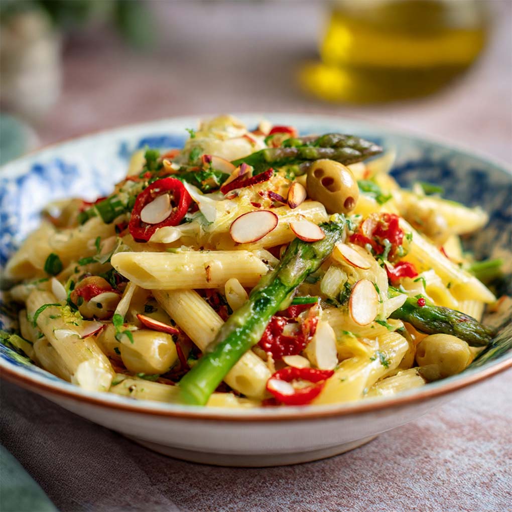 Mediterraner Pasta-Spargel-Salat mit grünem Spargel, Cherrytomaten, Oliven und Feta, serviert auf einem weißen Teller