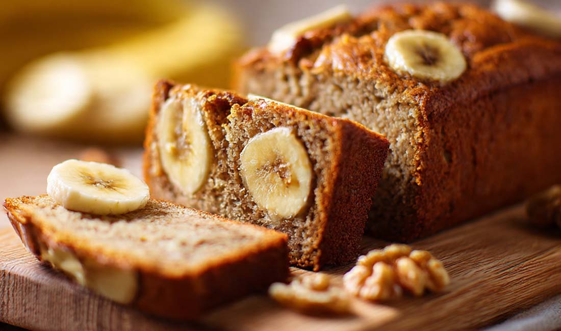 Ein detailreiches Food-Foto eines saftigen Bananenbrots ohne Zucker, aufgenommen in natürlichem Licht. Das goldbraune Bananenbrot liegt auf einem Holzbrett, umgeben von reifen Bananen und einer Tasse Kaffee. Ideal als Titelbild für den Blogbeitrag „Saftiges Bananenbrot ohne Zucker – Gesundes Rezept“ auf www.cucinarecipes.com .