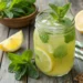 Glass of anti-inflammatory mint lemon juice with ice, garnished with fresh mint and lemon wheel on marble counter