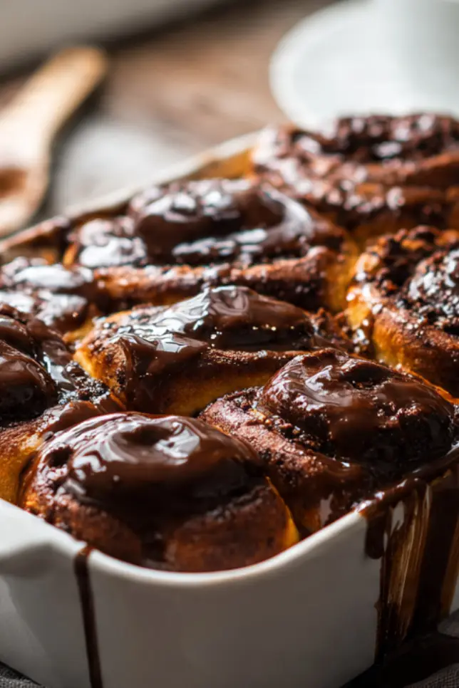 Freshly baked double chocolate rolls with chocolate glaze in white baking dish on rustic wooden table