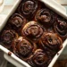 Freshly baked double chocolate rolls with chocolate glaze in white baking dish on rustic wooden table