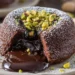 Pistachio chocolate lava cake with molten chocolate center flowing onto white plate garnished with crushed pistachios