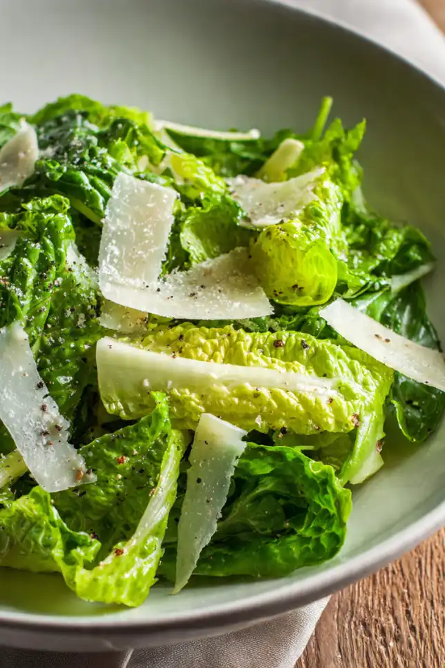 Simple green salad with fresh lettuce, olive oil dressing, and shaved Parmesan cheese in a white bowl