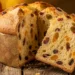 Golden homemade panettone in a paper mold sliced open on a rustic wooden table showing soft crumb with dried cranberries and candied orange peel, surrounded by fresh oranges and holiday decorations