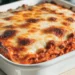 Freshly baked million dollar lasagna in a white ceramic dish with golden bubbly mozzarella on top and rich red meat sauce on the sides